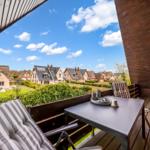 Terrace with table and chairs, view of houses and green areas under blue sky.