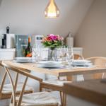 Dining table with four chairs, flowers, and glasses under a pendant light.