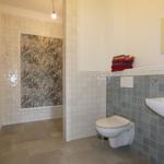 Badezimmer mit Dusche, Toilette und Waschbecken. Wand mit tropischen Motiv.