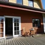 Terrasse mit Holztisch und Stühlen, Schiebetür zum Haus, rote Backsteinwand.