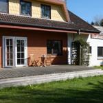 Haus mit Terrasse, Holzbank und Tisch. Fenster und Tür sind sichtbar.