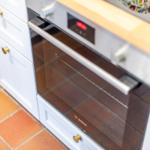 An integrated oven with glass door and control panel in a kitchen with white cabinets and wooden countertop.