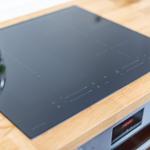 Induction cooktop on wooden surface with digital display and control elements.