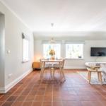 Dining area with table, chairs, and windows. Living area with sofa and TV.