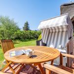 Terrace with wooden table, chair, and beach chair next to a house with thatched roof.