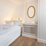 Schlafzimmer mit weißem Bett, Holzboden und runden Spiegel.
