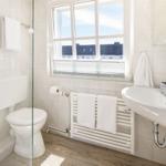 Badezimmer mit Toilette, Waschbecken und Fenster mit Blick auf Dächer.