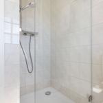 Dusche mit Glaswand und Handbrause, weiße Fliesen und Toilette sichtbar.