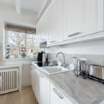 Küche mit weißen Schränken, grauem Arbeitsplatz und Fenster mit Blick draußen.