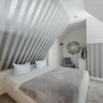 Schlafzimmer mit schräger Decke und gestreifter Wand. Bett, Kleiderschrank und Sessel sind vorhanden.