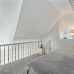 Schlafzimmer mit Dachschrägen, weißer Balustrade und Bett unter Fenster