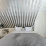 Schlafzimmer mit gestreifter Decke, weißem Bett und grauer Bettdecke.