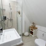 Badezimmer mit Dusche, Waschbecken und Toilette. Holzkommode mit Ankerdekoration.