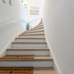 Eine Treppe mit Holzstufen und weißen Wänden. An der Wand hängt ein Bild.