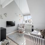 Wohnzimmer mit Sofa, Sessel, Fernseher und Fenster. Regal mit Gläsern und Dekoration.