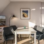 Esszimmer mit weißem Tisch, vier Stühlen und Fernseher an der Wand.
