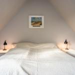 Schlafzimmer mit Dachschrägen, Bett mit weißer Bettwäsche und zwei Nachttischen mit Lampen.