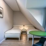 Zwei Einzelbetten, Nachttisch, grüner Tisch und Sessel in einem Dachzimmer.