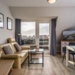 Wohnzimmer mit Sofa, Esstisch und TV. Balkon mit Blick auf Dächer.
