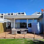 Deck with seating area and grill, adjacent lawn and modern building in background.