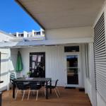 Terrace with table, chairs, and green umbrella under white roof.