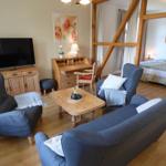 Wohnzimmer mit Sofa, Sessel und Fernseher. Im Hintergrund ist ein Schlafzimmer sichtbar.