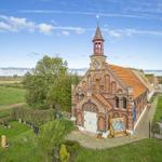 Historische Backstein-Kirche mit Turm und Friedhof, umgeben von grünen Wiesen und Bäumen.