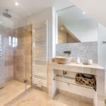 Dusche mit Glaswand, Waschbecken mit Spiegel und Heizkörper an der Wand.