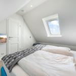 Schlafzimmer mit Dachfenster, Bett und Wandbild. Holztisch und weiße Türen.