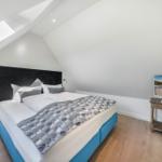 Schlafzimmer mit Doppelbett, TV und Holzboden unter schrägen Dachdecken.