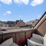 Balcony with two chairs overlooking houses and a clear blue sky.