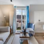 Wohnzimmer mit Sofa, Sessel und Terrasse. Hölzerner Boden und helle Wände.