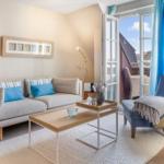 Wohnzimmer mit Sofa, Sessel und Tisch. Durchgehende Glastür führt auf Balkon.