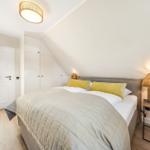 Schlafzimmer mit Dachschrägen, Bett mit Kissen, Nachttisch und Lampe.