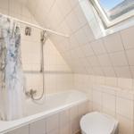 Badezimmer mit Dusche, Toilette und Dachfenster. Fliesenwand und Badewanne.