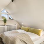 Schlafzimmer mit Dachschrägen, Fenster und Bett mit Kissen.