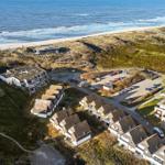 Strandnahe Ferienhäuser mit Parkplatz und Dünenlandschaft.