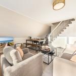 Wohnbereich mit Sofa, Sessel und Essbereich unter Dachschräge. Treppenhaus führt nach oben.