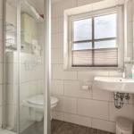 Badezimmer mit Dusche, Toilette, Waschbecken und Fenster mit Jalousie.