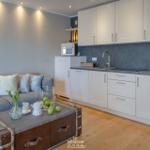 Wohnbereich mit Sofa, Kühlschrank und Küchenzeile. Holzboden und Wandbild mit Strandmotiv.