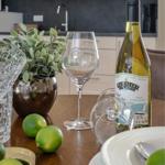 Tisch mit Weinglas, Flasche, Zitrusfrüchten und Pflanze in Küche.