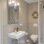Badezimmer mit Dusche, Waschbecken und Toilette. Holzschrank und Spiegel mit Licht.