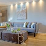 Wohnzimmer mit Sofa, Kaffeetisch und Küchenbereich. Wandbild und Holzboden.