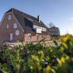 Ein zweistöckiges Haus mit Backsteinfassade und dunklem Dach. Vorgarten mit Sträuchern.