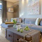 Ein Wohnzimmer mit grauem Sofa, Holzboden und einem Koffer als Couchtisch.