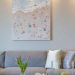 Ein Sofa mit Kissen, eine Vase mit Tulpen und ein Bild an der Wand.