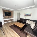 Wohnzimmer mit Sofa, Couchtisch und Fernseher an Holzwand.