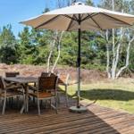 Holztisch mit Stühlen unter einem Sonnenschirm auf einer Terrasse im Wald.