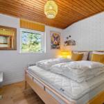 Schlafzimmer mit weißem Bett, Holzdecke und Fenster mit Blick auf Bäume.