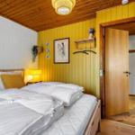 Schlafzimmer mit Bett, gelber Wand und Holzdecke. Tür führt in einen Flur.